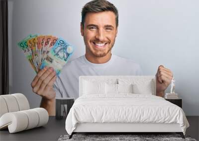 Handsome caucasian man holding australian dollars screaming proud, celebrating victory and success very excited with raised arm Wall mural