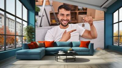 Handsome hispanic man holding keys of new home smiling happy pointing with hand and finger Wall mural