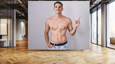 Handsome hispanic man standing shirtless with a big smile on face, pointing with hand finger to the side looking at the camera. Wall mural