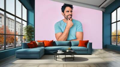 Handsome hispanic man with beard wearing casual clothes with hand on chin thinking about question, pensive expression. smiling with thoughtful face. doubt concept. Wall mural