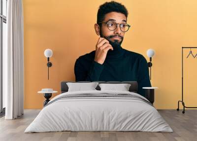 Handsome hispanic man with beard wearing turtleneck sweater thinking concentrated about doubt with finger on chin and looking up wondering Wall mural