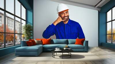 Handsome indian worker man wearing uniform and helmet over isolated white background smiling doing phone gesture with hand and fingers like talking on the telephone. Communicating concepts. Wall mural