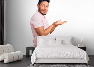 Handsome latin american young man wearing casual summer shirt pointing aside with hands open palms showing copy space, presenting advertisement smiling excited happy Wall mural