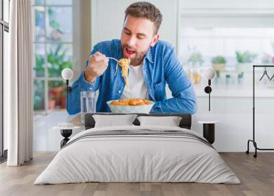 Handsome man eating pasta with meatballs and tomato sauce at home while smiling at the camera Wall mural