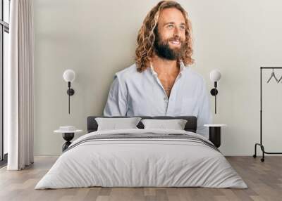 Handsome man with beard and long hair wearing casual white shirt looking to side, relax profile pose with natural face and confident smile. Wall mural