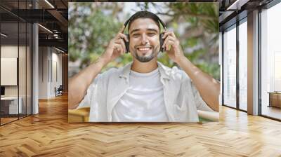 Handsome man with beard enjoying music on headphones outdoors in a sunny green park Wall mural