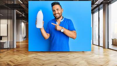 Handsome man with beard holding liter bottle of milk smiling happy pointing with hand and finger Wall mural