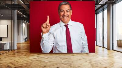 Handsome middle age businessman standing over isolated red background showing and pointing up with finger number one while smiling confident and happy. Wall mural