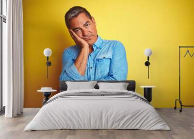 Handsome middle age man wearing denim shirt standing over isolated yellow background thinking looking tired and bored with depression problems with crossed arms. Wall mural