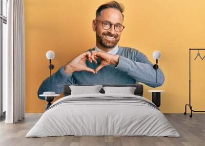 Handsome middle age man wearing glasses smiling in love doing heart symbol shape with hands. romantic concept. Wall mural