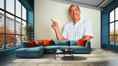 Handsome middle age man wearing polo standing over isolated white background with a big smile on face, pointing with hand and finger to the side looking at the camera. Wall mural