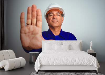 Handsome middle age worker man wearing uniform and helmet over isolated white background doing stop sing with palm of the hand. Warning expression with negative and serious gesture on the face. Wall mural