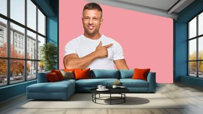 Handsome muscle man wearing casual white tshirt cheerful with a smile on face pointing with hand and finger up to the side with happy and natural expression Wall mural