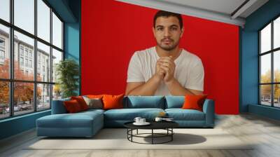 Handsome young hispanic man in a white shirt stands against an isolated red background Wall mural