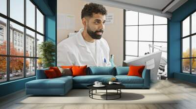 Handsome young hispanic man in labcoat working with computer in modern laboratory Wall mural