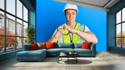 Handsome young man wearing safety helmet and reflective jacket smiling in love showing heart symbol and shape with hands. romantic concept. Wall mural