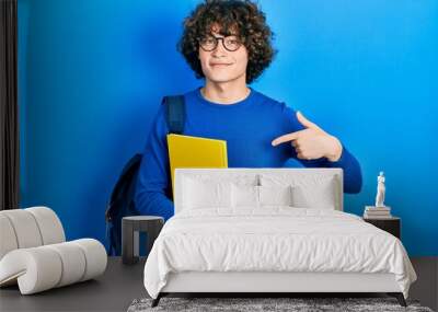 Handsome young man wearing student backpack and holding book pointing finger to one self smiling happy and proud Wall mural