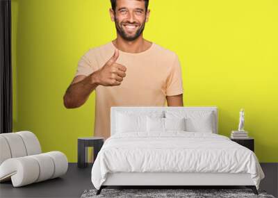 Handsome young man with beard wearing casual tshirt doing happy thumbs up gesture with hand. approving expression looking at the camera showing success. Wall mural