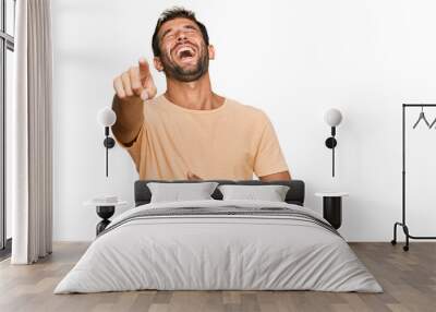 Handsome young man with beard wearing casual tshirt laughing at you, pointing finger to the camera with hand over body, shame expression Wall mural