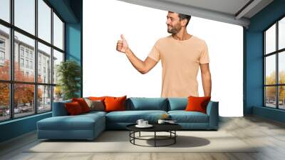 Handsome young man with beard wearing casual tshirt looking proud, smiling doing thumbs up gesture to the side Wall mural