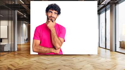 Handsome young man with curly hair and bear wearing casual pink tshirt with hand on chin thinking about question, pensive expression. smiling with thoughtful face. doubt concept. Wall mural