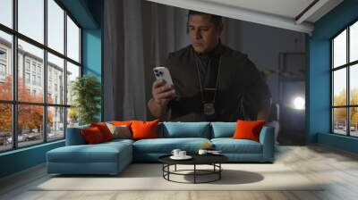 Hispanic detective man inspects crime scene indoors using smartphone for evidence collection Wall mural