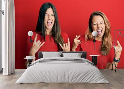 Hispanic family of mother and daughter wearing casual clothes over red background shouting with crazy expression doing rock symbol with hands up. music star. heavy music concept. Wall mural