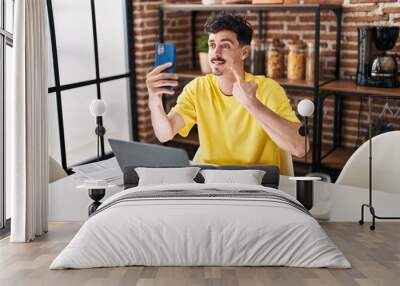 Hispanic man doing video call with smartphone smiling happy pointing with hand and finger Wall mural