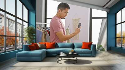 Hispanic man texting in a modern indoor room with clothes rack and mirror Wall mural