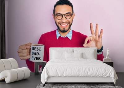 Hispanic man with beard drinking mug of coffee with best dad ever message doing ok sign with fingers, smiling friendly gesturing excellent symbol Wall mural