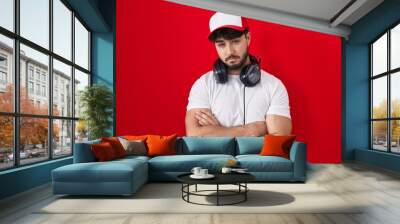 Hispanic man with beard wearing gamer hat and headphones looking sleepy and tired, exhausted for fatigue and hangover, lazy eyes in the morning. Wall mural