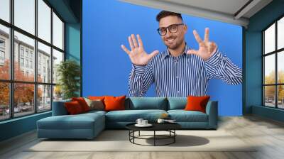 Hispanic man with beard wearing glasses showing and pointing up with fingers number eight while smiling confident and happy. Wall mural