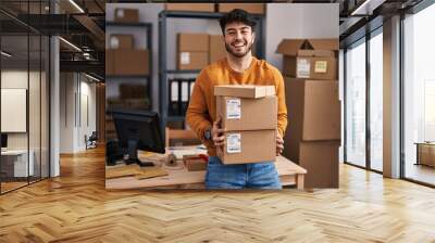 Hispanic man with beard working at small business ecommerce holding packages celebrating crazy and amazed for success with open eyes screaming excited. Wall mural