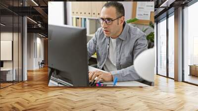 Hispanic man working concentrated at his desk in a well-lit modern office, using a computer and wearing casual attire Wall mural