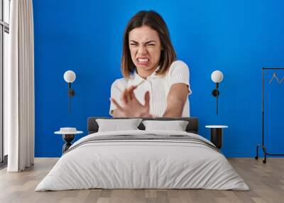 Hispanic woman standing over blue background disgusted expression, displeased and fearful doing disgust face because aversion reaction. with hands raised Wall mural