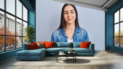 Hispanic woman standing over blue background relaxed with serious expression on face. simple and natural looking at the camera. Wall mural