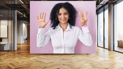 Hispanic woman with curly hair standing over pink background showing and pointing up with fingers number eight while smiling confident and happy. Wall mural