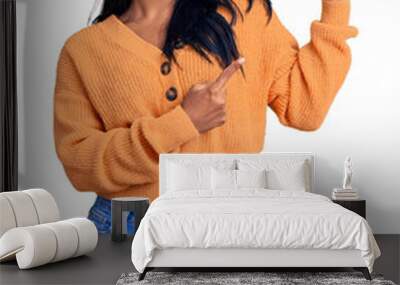 Hispanic woman with long hair wearing casual winter sweater smiling and looking at the camera pointing with two hands and fingers to the side. Wall mural