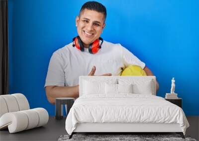 Hispanic young man holding hardhat smiling happy pointing with hand and finger Wall mural