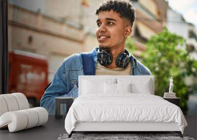 Hispanic young man smiling wearing headphones at the street Wall mural