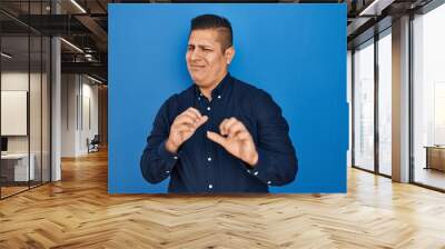 Hispanic young man standing over blue background disgusted expression, displeased and fearful doing disgust face because aversion reaction. with hands raised Wall mural