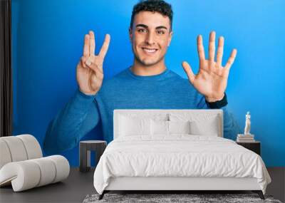 Hispanic young man wearing casual winter sweater showing and pointing up with fingers number eight while smiling confident and happy. Wall mural