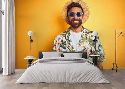 Indian man on vacation wearing floral shirt hat sunglasses over isolated yellow background with a happy and cool smile on face. Lucky person. Wall mural