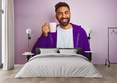 Indian man wearing purple sweatshirt drinking cup of coffee over isolated pink background with a happy face standing and smiling with a confident smile showing teeth Wall mural