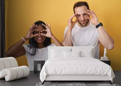 Interracial couple standing over yellow background trying to open eyes with fingers, sleepy and tired for morning fatigue Wall mural