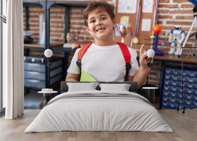 Little hispanic boy wearing student backpack and holding book at school class smiling with an idea or question pointing finger with happy face, number one Wall mural