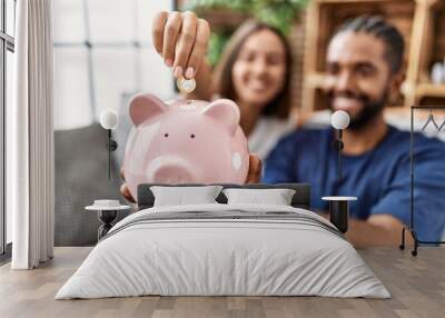 Man and woman couple smiling confident insert coin on piggy bank at home Wall mural