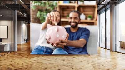 Man and woman couple smiling confident insert coin on piggy bank at home Wall mural