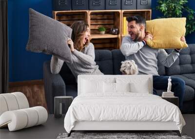 Man and woman fighting with cushion sitting on sofa with dog at home Wall mural