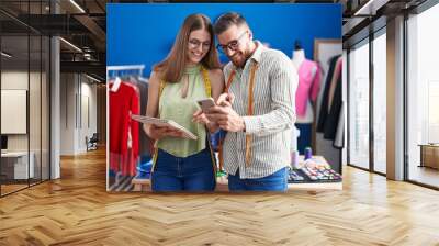 Man and woman tailors using smartphone holding notebook at clothing factory Wall mural